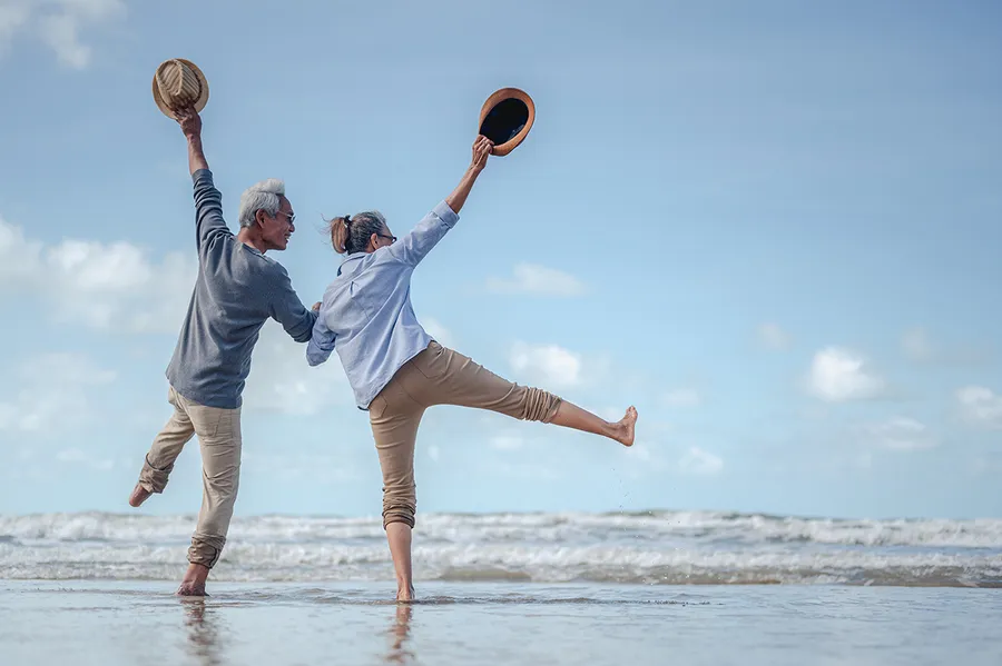 Pareja jubilada jugando descalza en la orilla del mar tras preparar su jubilación